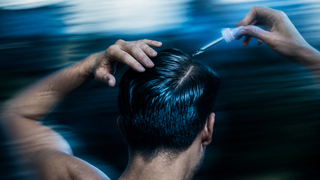Person applying adegen hair growth serum hair with a dropper, against a blurred water background